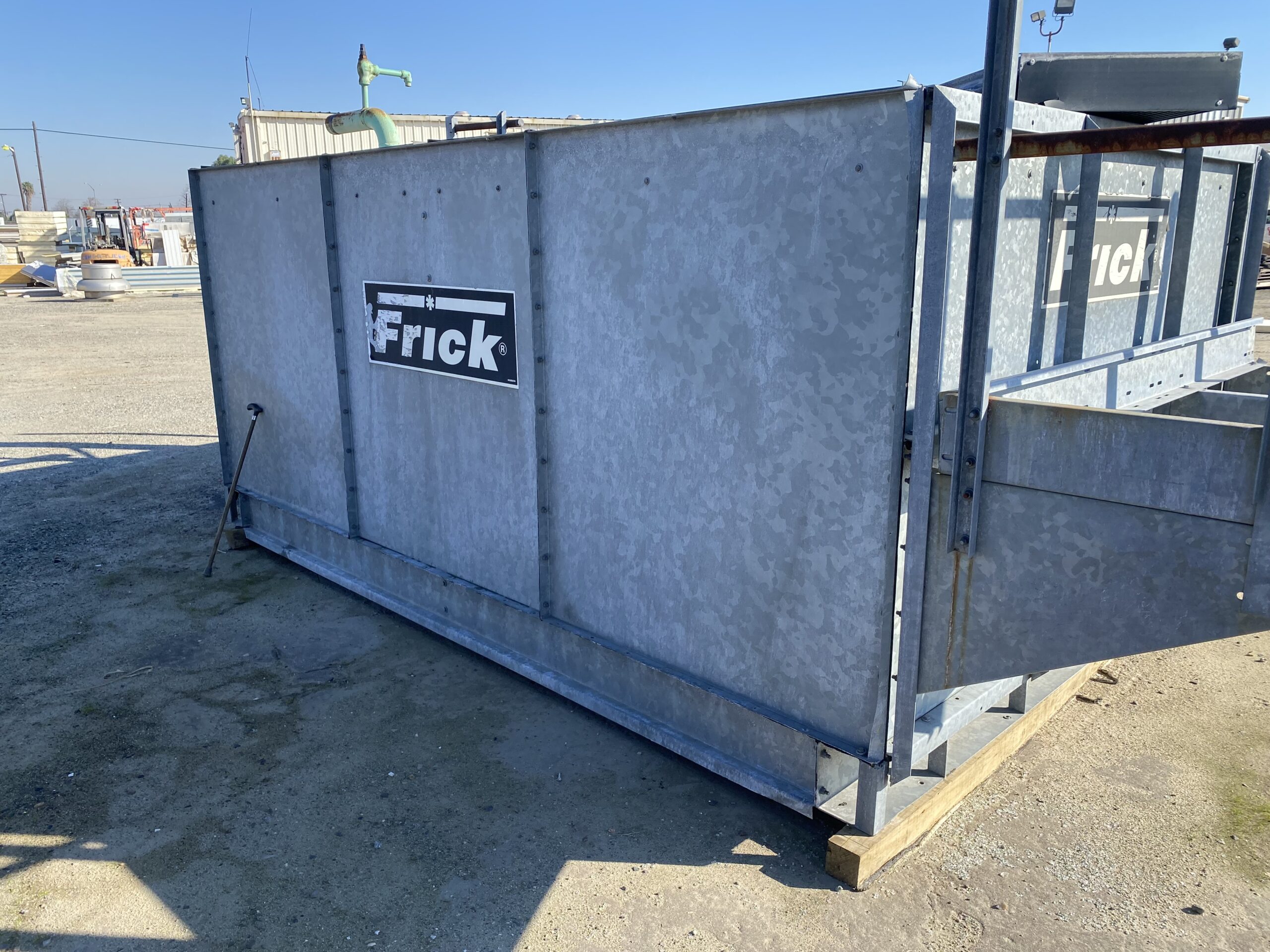 Large galvanized Frick industrial unit in an outdoor construction yard with gravel ground and steel framing nearby.