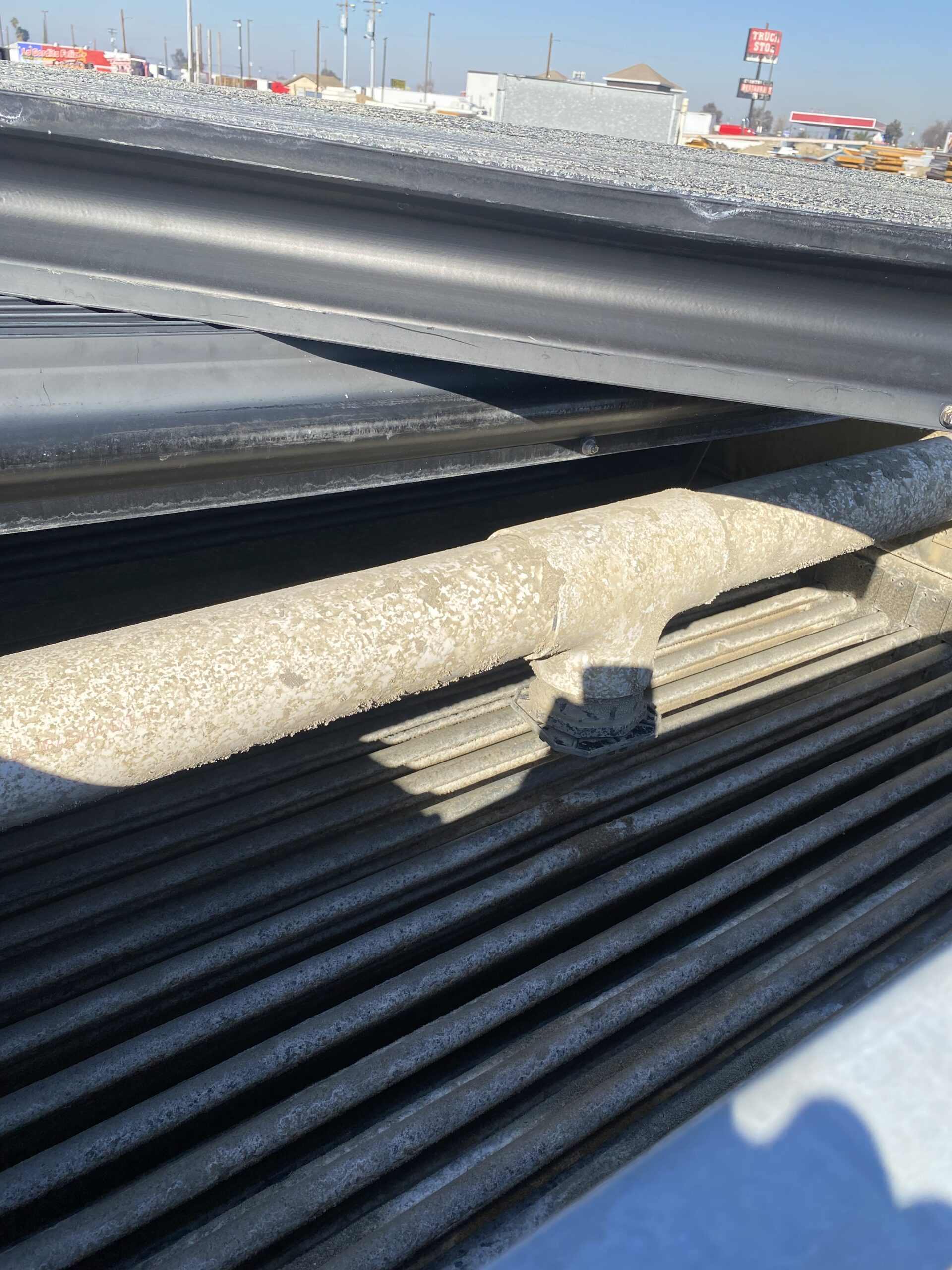 Close-up of weathered, stacked metal beams in an outdoor industrial yard, showing rust and dust on the rails under a blue sky.