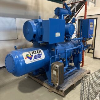 Blue industrial refrigeration compressor unit (Vilter) mounted on a wooden pallet in a workshop. the large cylindrical tank and piping are visible as part of the system.