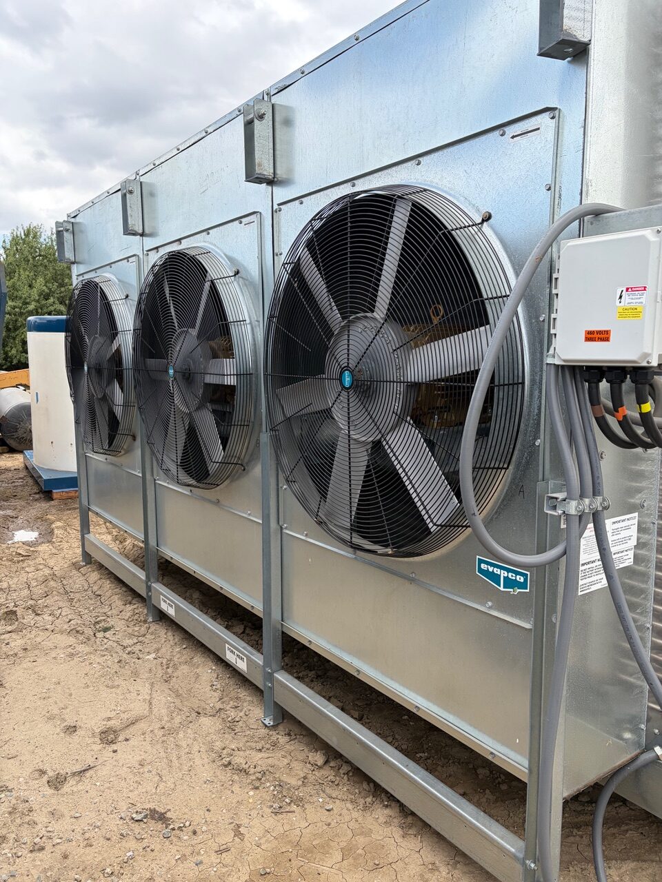 Outdoor industrial HVAC condenser with three large protective fans and metal enclosure.