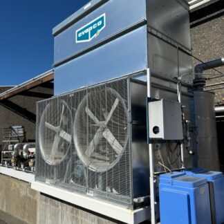 Industrial HVAC unit with large fan blades behind a metal grille, labeled Evapco, outdoors on a concrete platform against a blue sky.