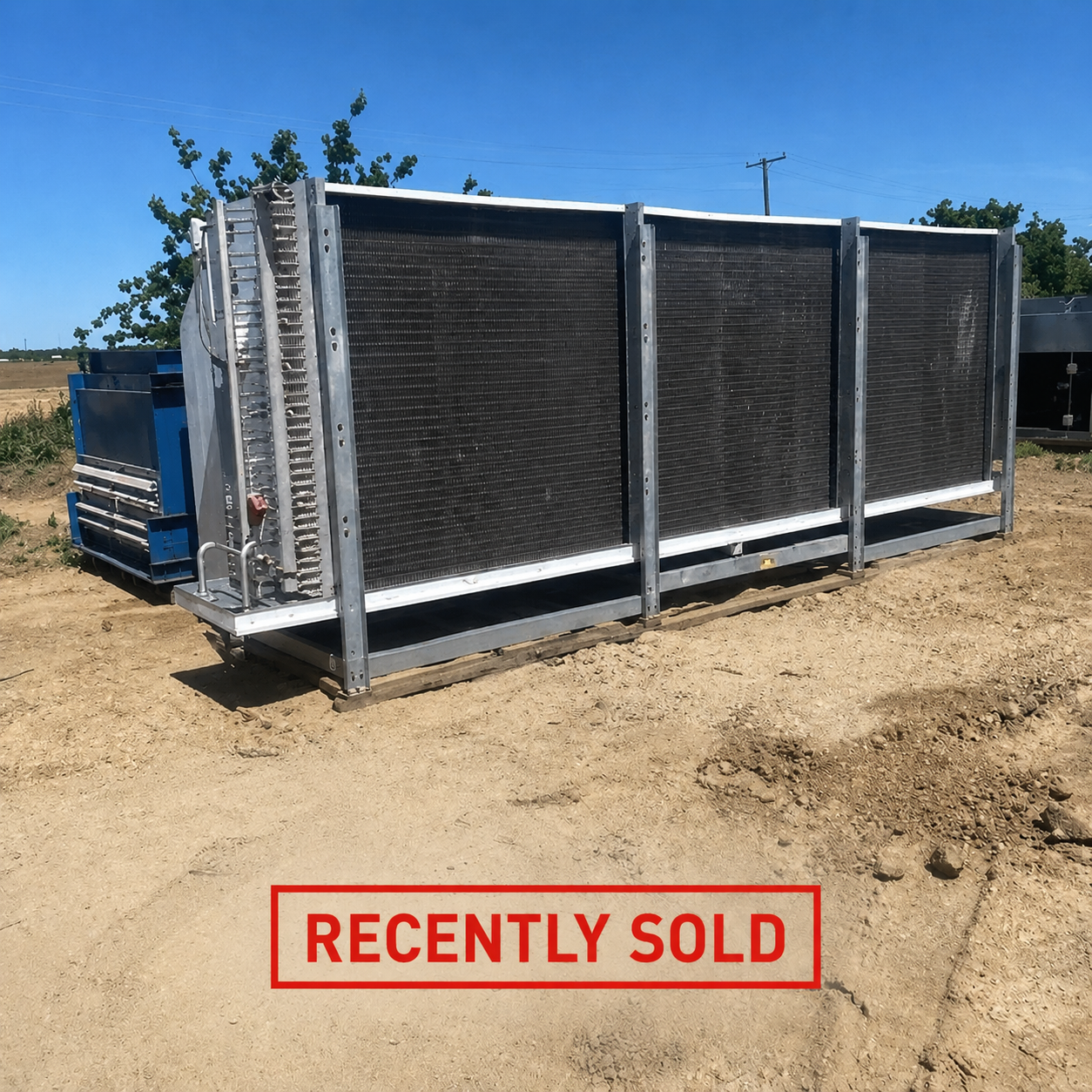 Large industrial radiator/heat-exchanger unit on a dirt lot, with a blue machine nearby and a red 'RECENTLY SOLD' stamp at the bottom.