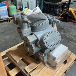 Industrial hydraulic pump on a wooden pallet in a warehouse, with hoses and gauges nearby, ready for installation or transport.