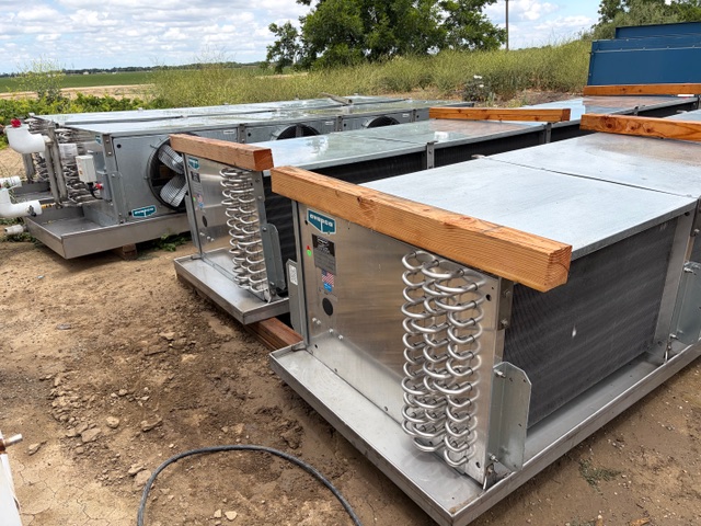 Industrial HVAC air handler units on a dirt site, with metal casings, coils visible and wooden supports on top.