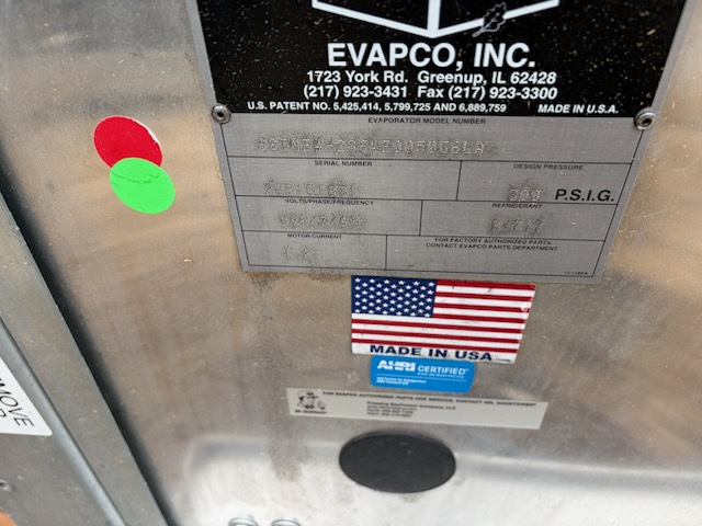 Metal HVAC unit panel with EVAPCO, Inc. data plate and a Made in USA sticker; two colored decals (red and green) are visible at left and an American flag label beneath the data plate.