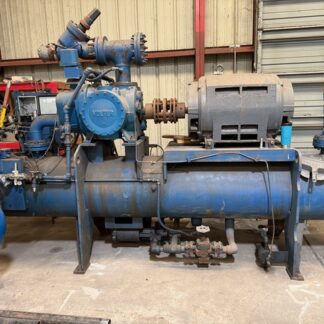 Large blue industrial pump and compressor system with a motor, valves, and piping in a workshop setting on a concrete floor