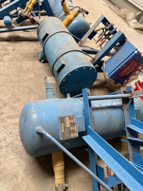 Blue industrial air compressor system with cylindrical tanks and mounting frame on a concrete floor.