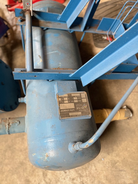 Blue industrial electric motor mounted on a metal frame in a workshop, with a visible nameplate and wiring