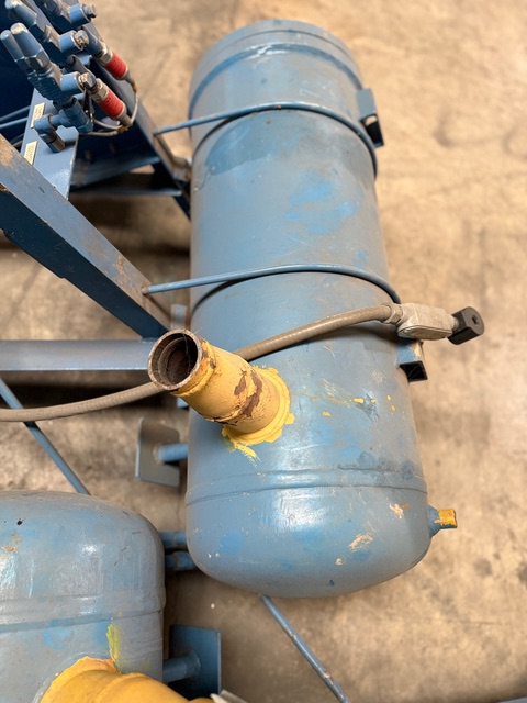 Blue cylindrical industrial tank with an open pipe fitting and yellow seal, on a workshop floor with surrounding wires and components.