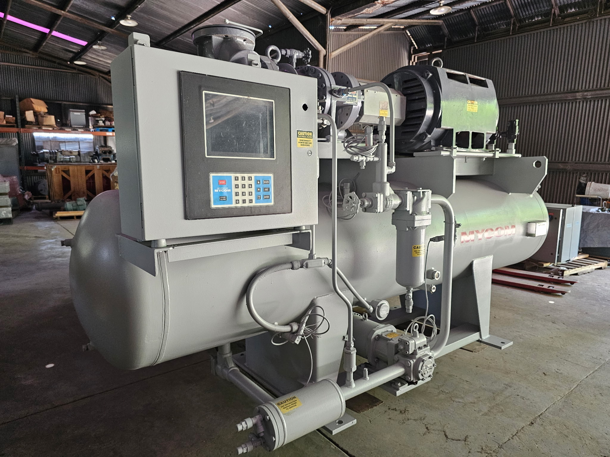 Large industrial machine with control panel, pipes, and a big green motor in a warehouse setting.
