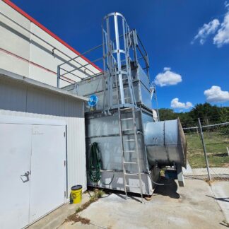 Outdoor industrial HVAC/ventilation unit with metal framework and large ductwork beside a building, under a bright blue sky.