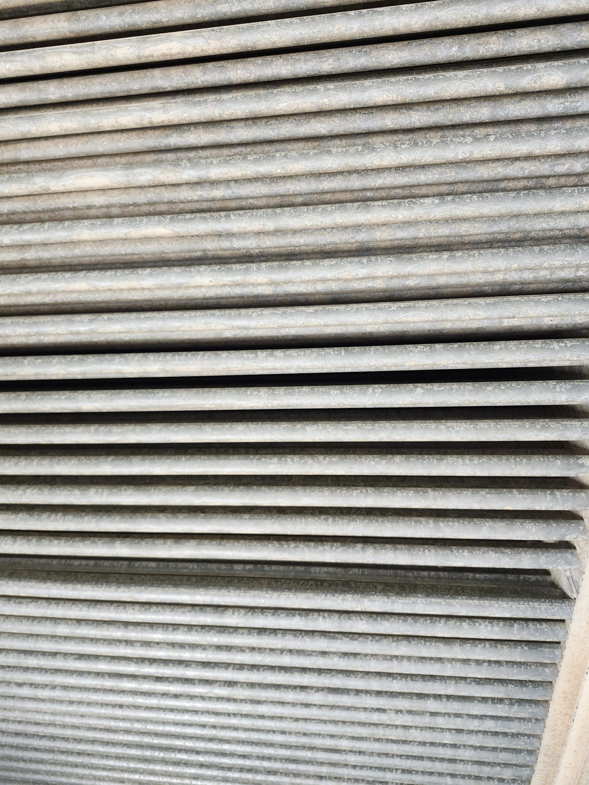 Close-up of weathered gray corrugated metal sheets with horizontal ridges and dusty texture/oxide specks.