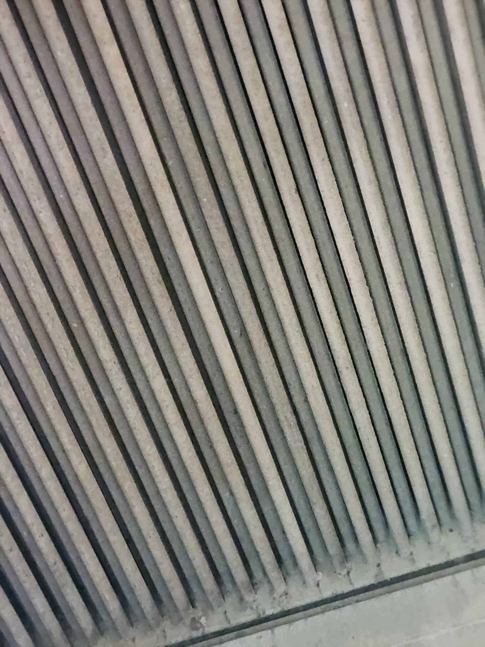 Close-up of dusty, diagonal metal slats (like blinds or a vent) with a repeating pattern.