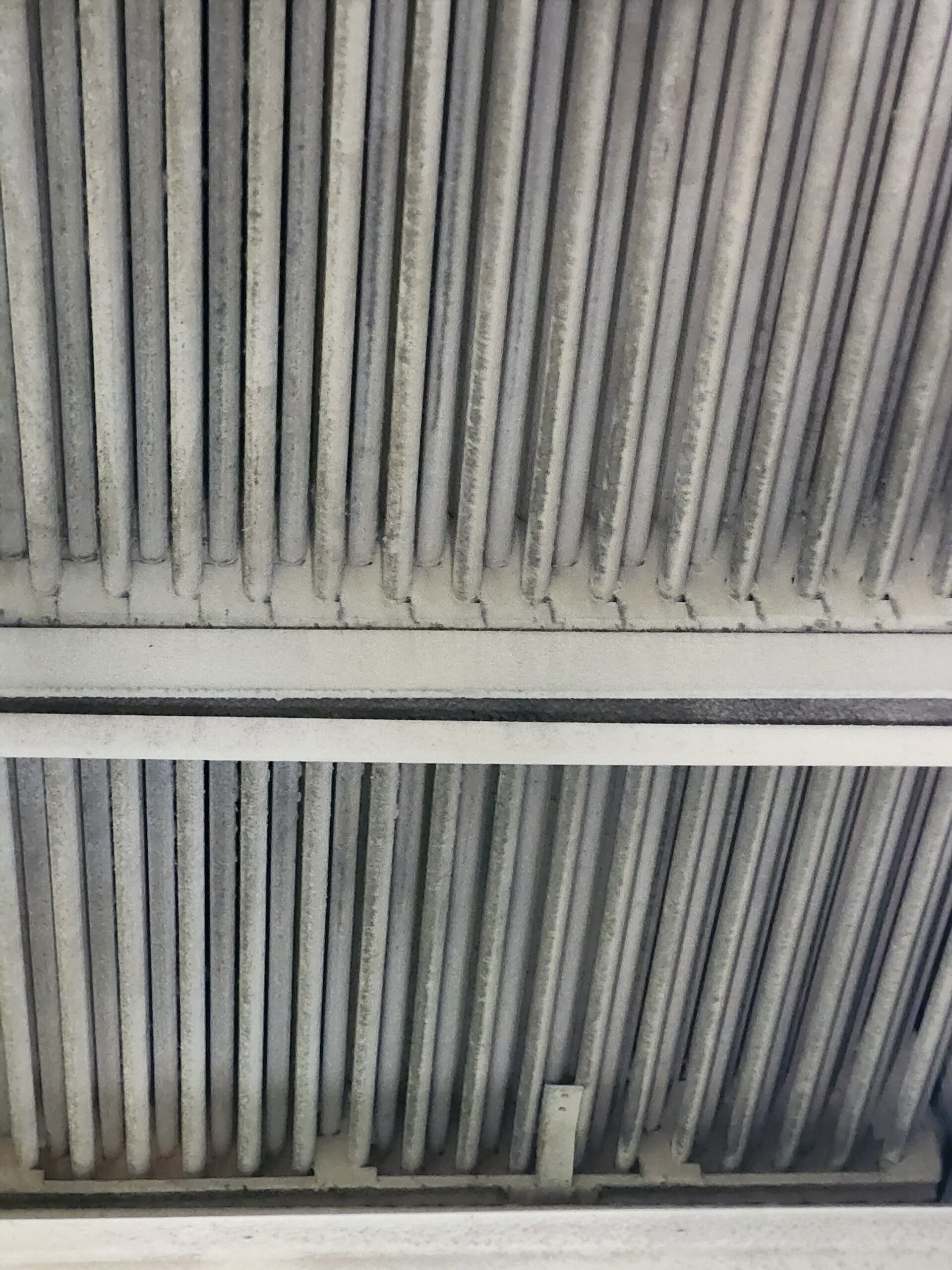 Close-up of dusty vertical metal fins from an industrial vent or radiator.