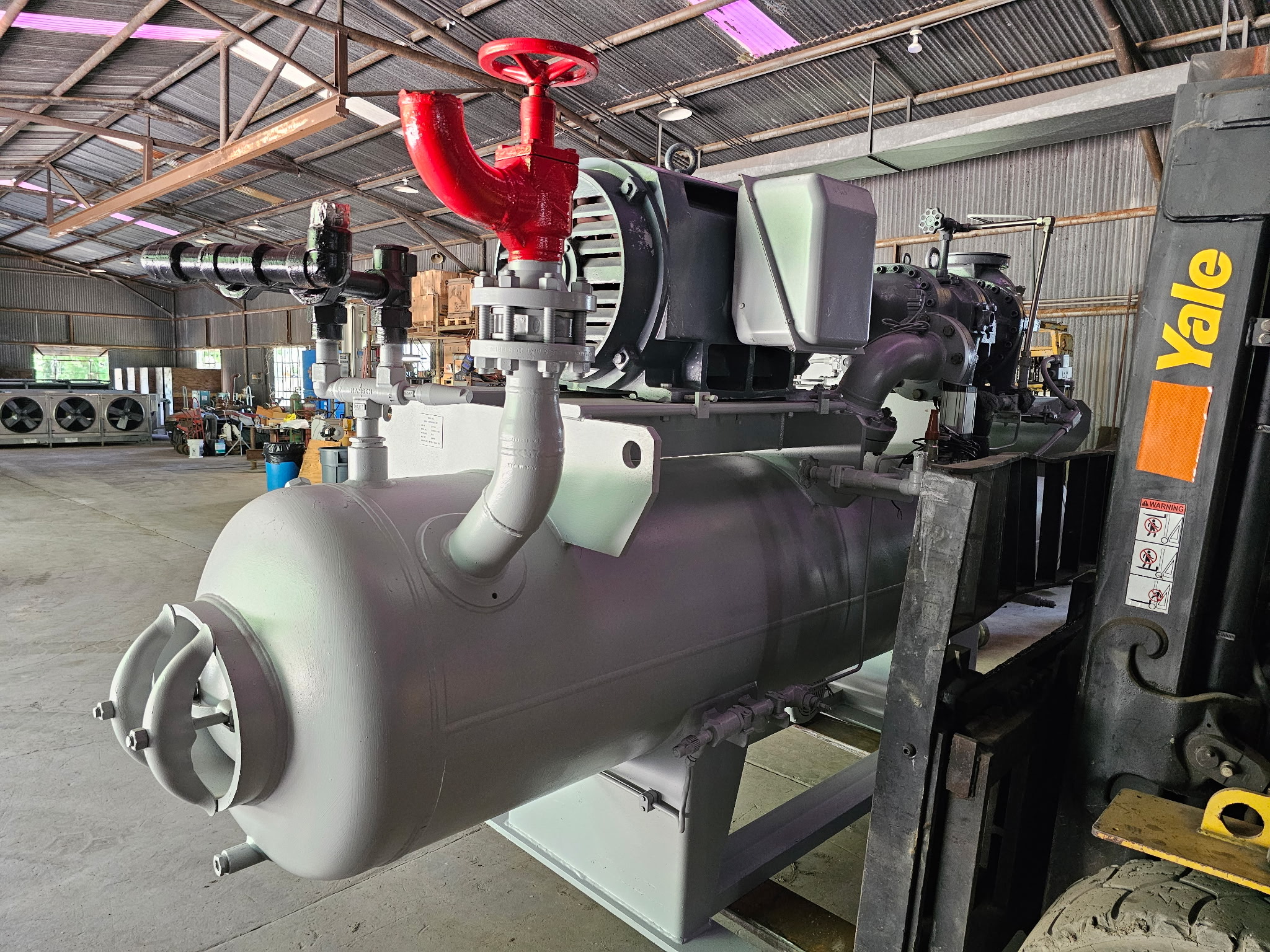 Industrial pump system with a large red valve and gray cylindrical vessel in a warehouse setting