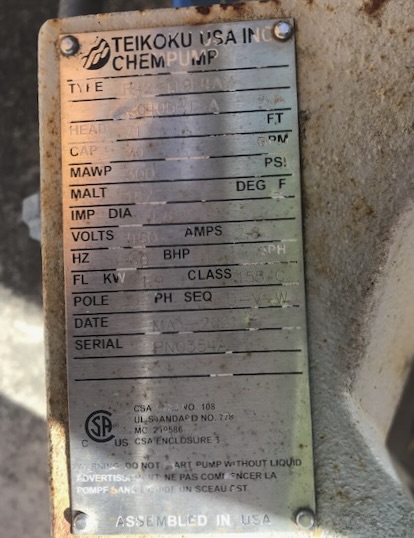 Close-up of a rusted metal pump nameplate labeled Teikoku USA Inc Pump, showing model fields, volts, amps, HP, date, and serial number (textual data partially worn).
