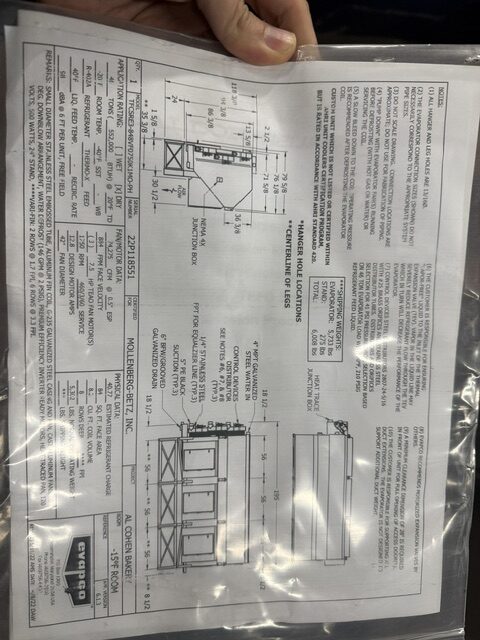 Rotated photo of a printed technical specification sheet with diagrams and measurements for a cabinet/rack, held by a hand.