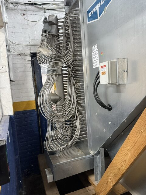 Industrial air handling unit with coiled metal ducts and a metal control panel in a utility room.