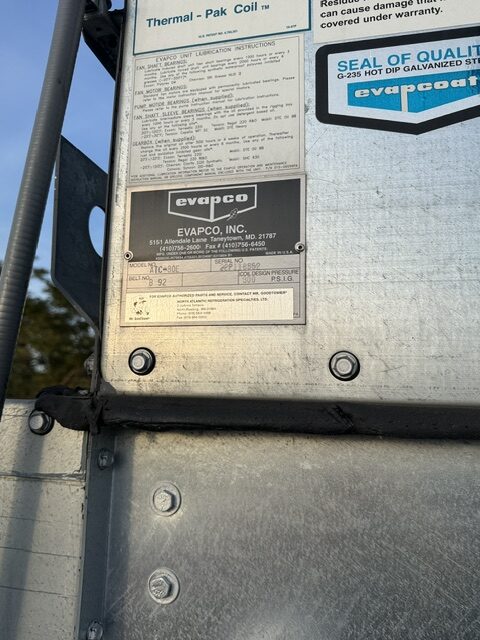 Close-up of a metal industrial unit with Evapco nameplates and instruction labels visible on the panel.
