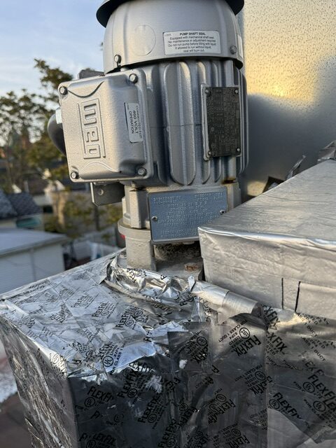 Outdoor rooftop HVAC unit: close-up of a metal pump motor attached to ductwork with foil tape.