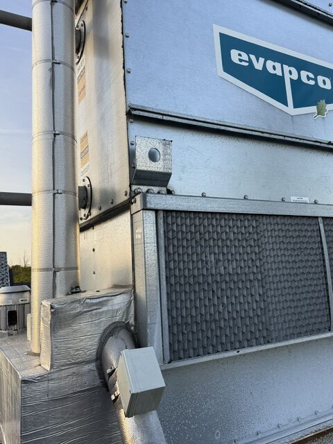 Close-up of an Evapco HVAC cooling unit on a rooftop, showing metal casing, ductwork, and a small square electrical box.