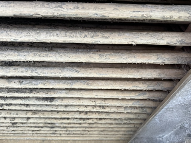 Dusty horizontal vent louvers with grime and buildup at an industrial ceiling edge, close-up view.