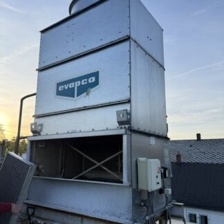 Rooftop industrial cooling tower with an Evapco logo, metal panels, and wiring on a steel frame at sunset.