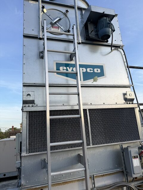 Industrial cooling tower unit with Evapco logo, metal casing, and an access ladder outdoors under a blue sky.