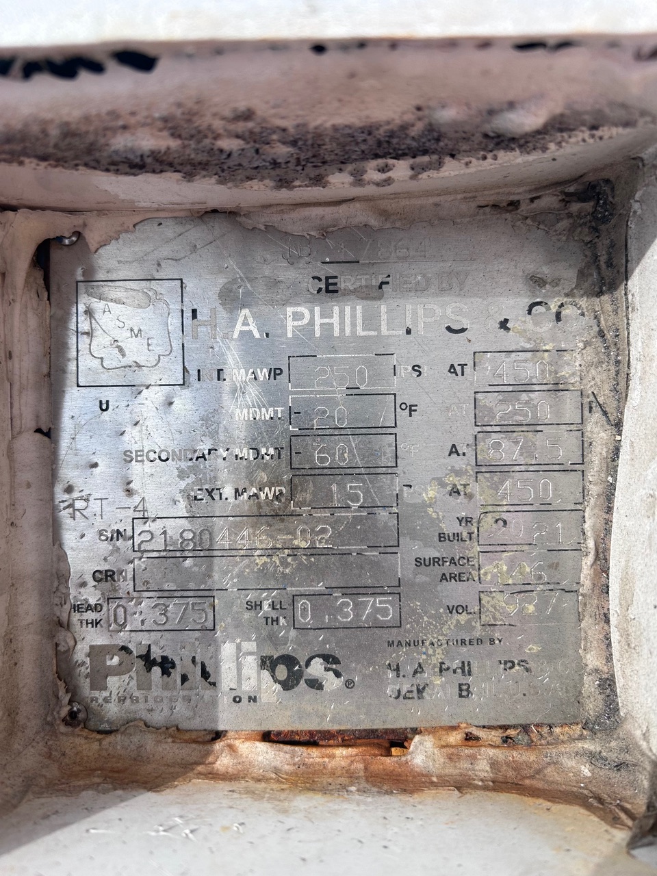 Close-up of a weathered metal equipment nameplate with engraved specifications and an ASME/ASME-like logo, showing rows of technical data (MAWP, MDMT, etc.).