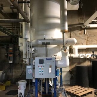 Blue skid-mounted control panel in a mechanical room, surrounded by white pipes and a tall cylindrical vessel behind it.