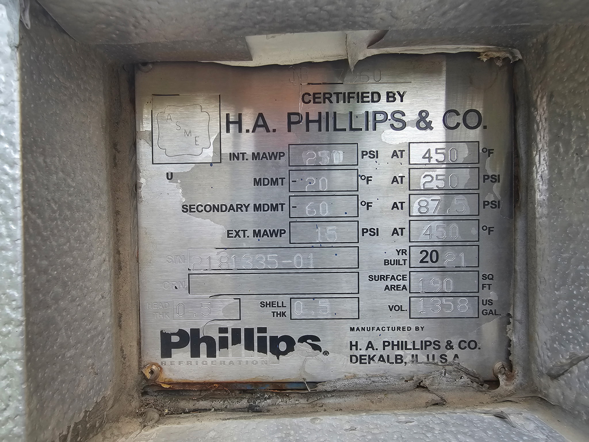 Metal certification plate inside a dusty refrigeration housing showing 'CERTIFIED BY H.A. PHILLIPS & CO.' and its pressure/temperature datas.