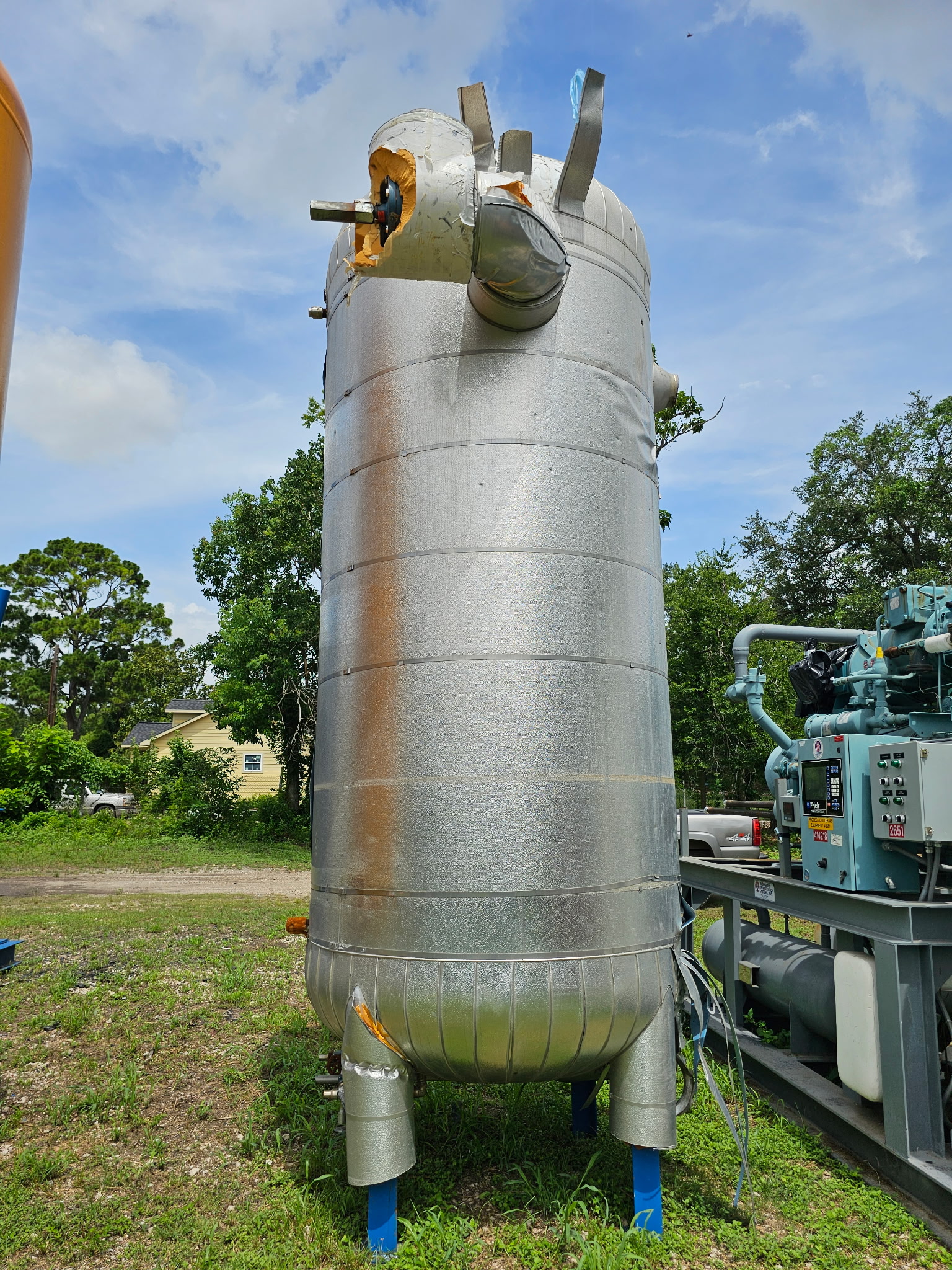 Industrial metal vertical silo with insulated elbow pipe and damaged top cover outdoors near machinery