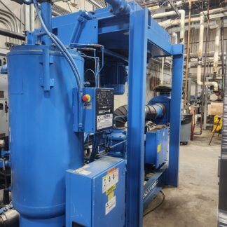 Blue industrial machinery with a large vertical tank and network of pipes in a factory utility room.