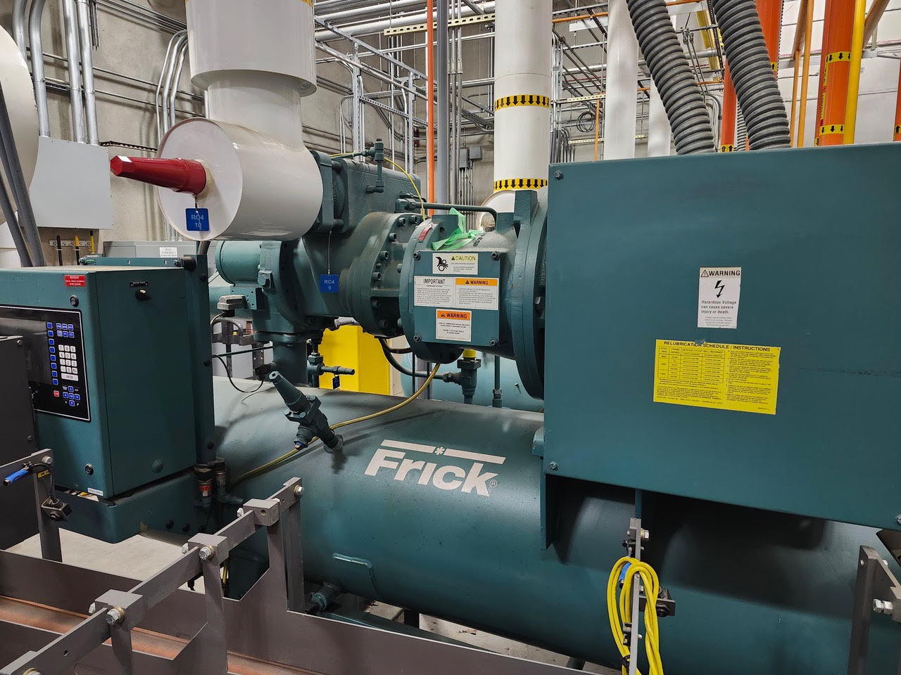 Large Frick generator in a mechanical room with pipes, control panel, and warning labels visible.