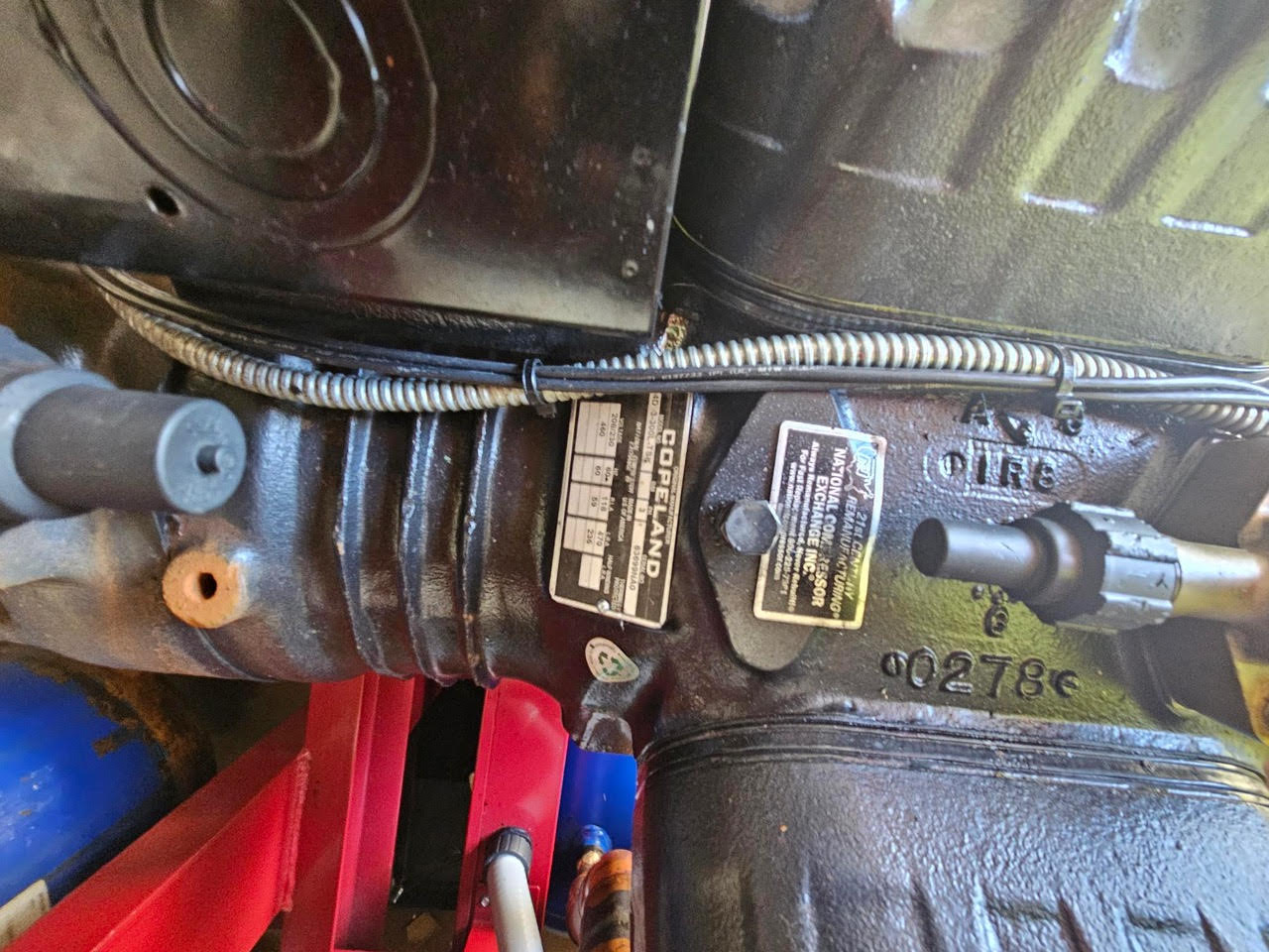 Close-up of a Copeland compressor with nameplate, mounted on a machine, with electrical conduit above.