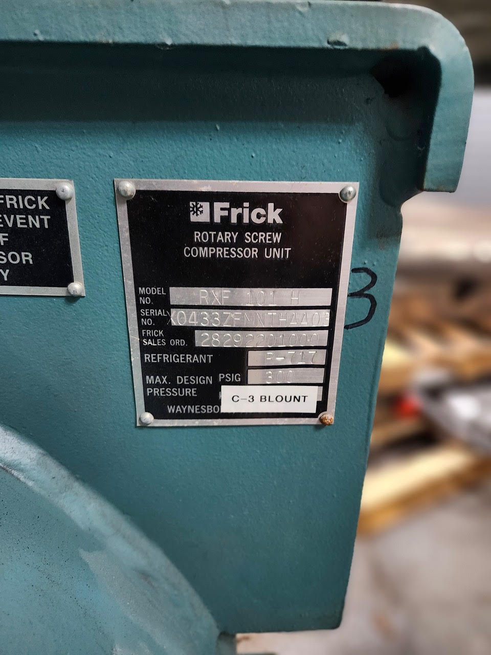 Frick rotary screw compressor nameplate on a teal machine, showing model RXF101H and serial number (close-up).