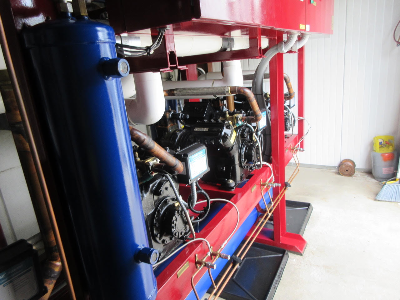 Industrial generator or engine mounted on a red frame with a blue vertical tank, copper pipes, and wiring in a workshop setting.