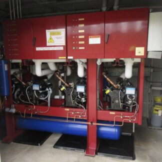 Two red industrial chiller units with white piping, pumps, and a blue reservoir beneath in a mechanical room.