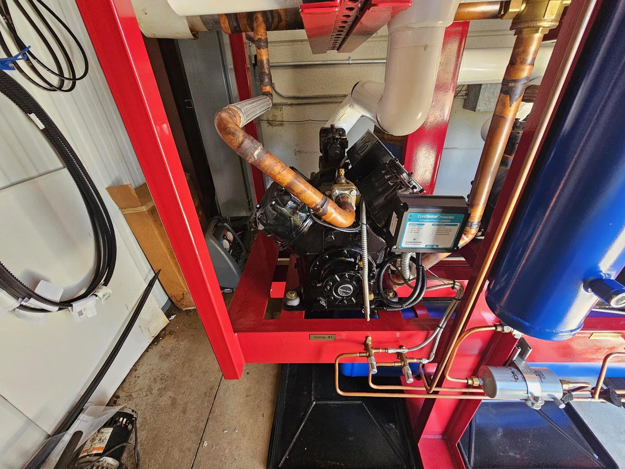 Industrial mechanical assembly with copper pipes and a black engine on a red frame; visible control box labeled CoreSense nearby.