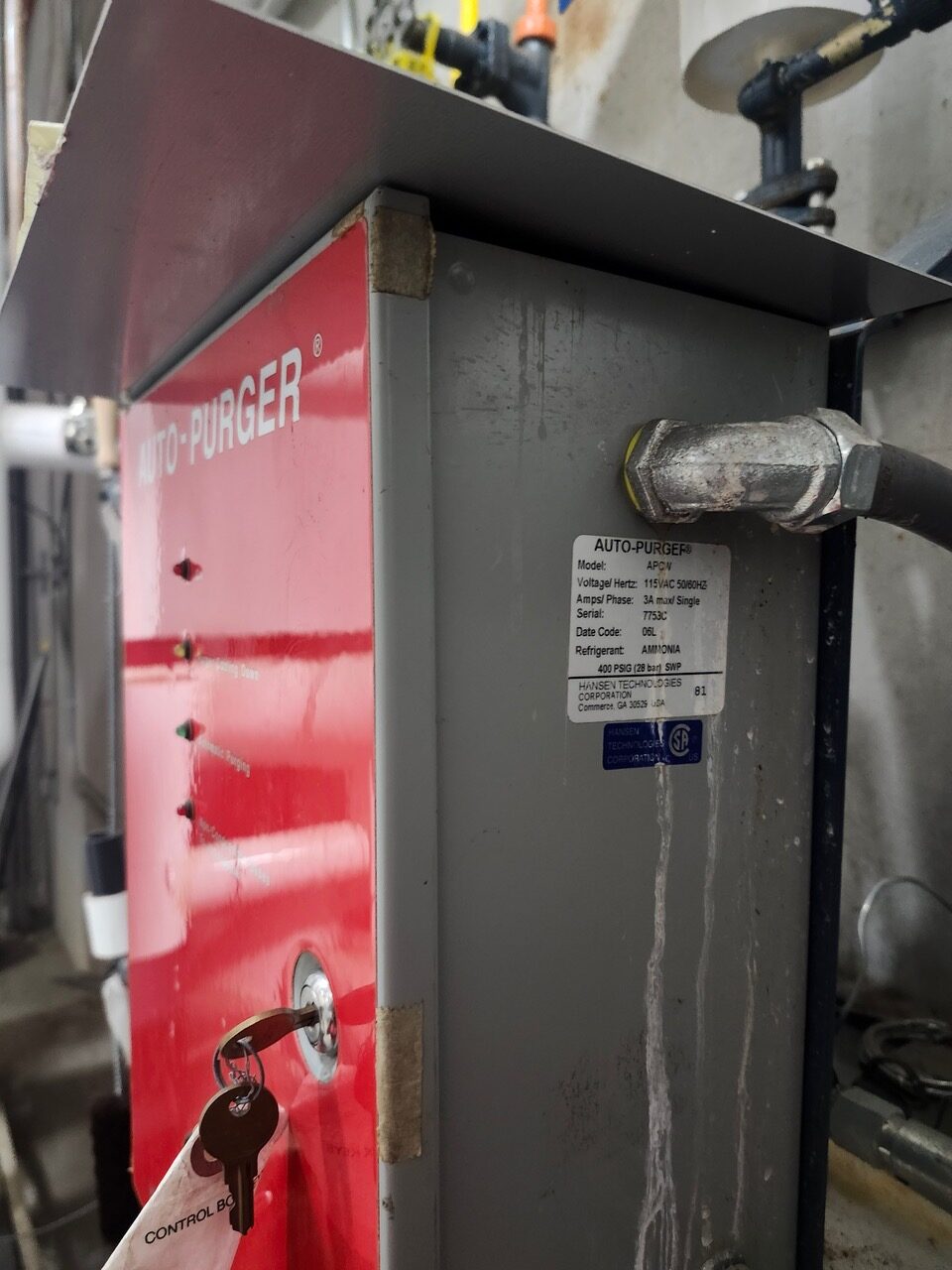 Auto-Purger unit in a mechanical room: red panel, grey body, key in the lock, and a data plate visible.
