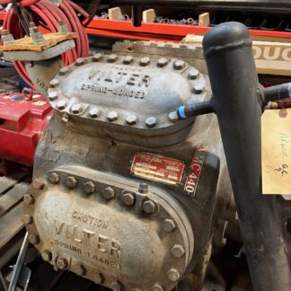 Industrial Vilter spring-loaded valve with bolted circular cover; red cables and workshop tools nearby.