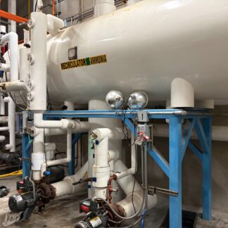 Horizontal ammonia recirculator vessel mounted on a blue steel frame, surrounded by white piping and valves in an industrial plant.