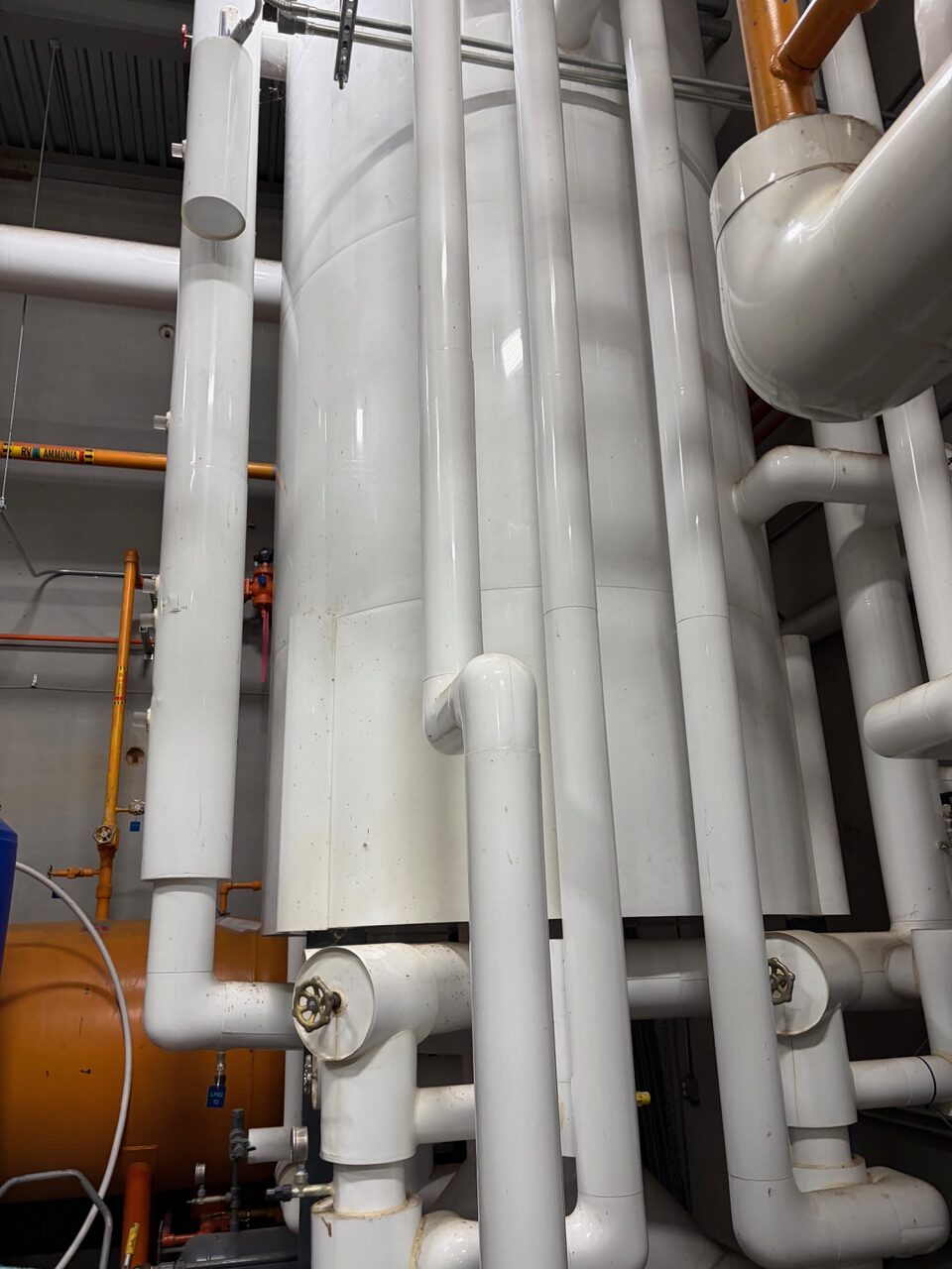 Industrial boiler room with white pipes, valves, and orange gas line in the background.