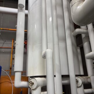 Industrial piping system with multiple white vertical pipes, valves, and a large central tank; orange gas lines in the background.