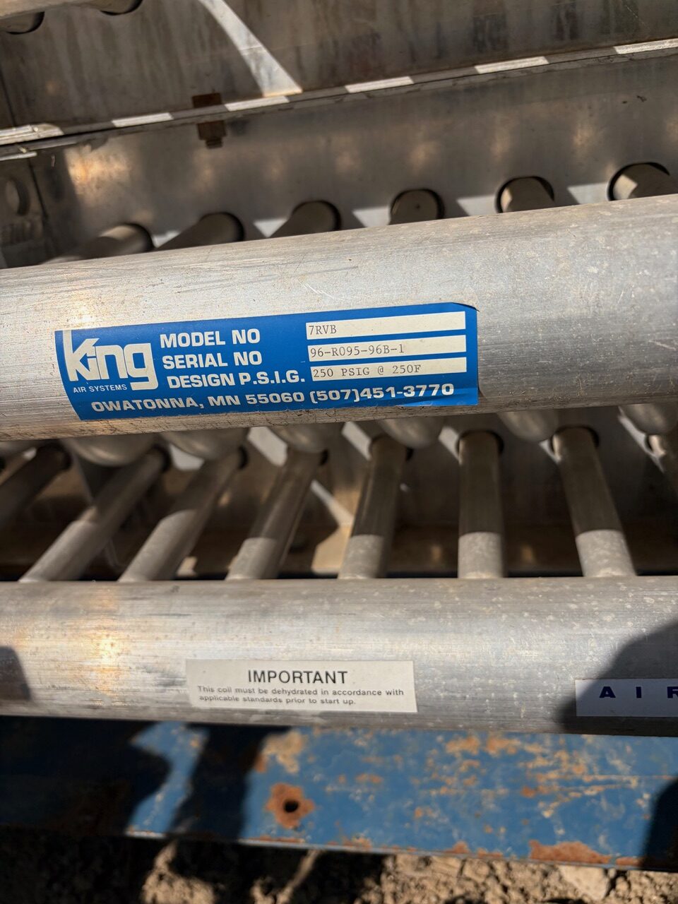 Blue label on a metal agricultural machine component reading King Air Systems and model/serial details (7RVB, 96-R095-96B-1).