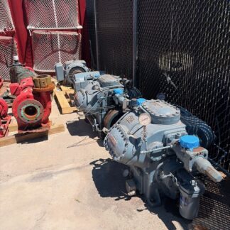 Industrial pump or compressor unit with blue covers, outdoors beside a chain-link fence and red storage containers