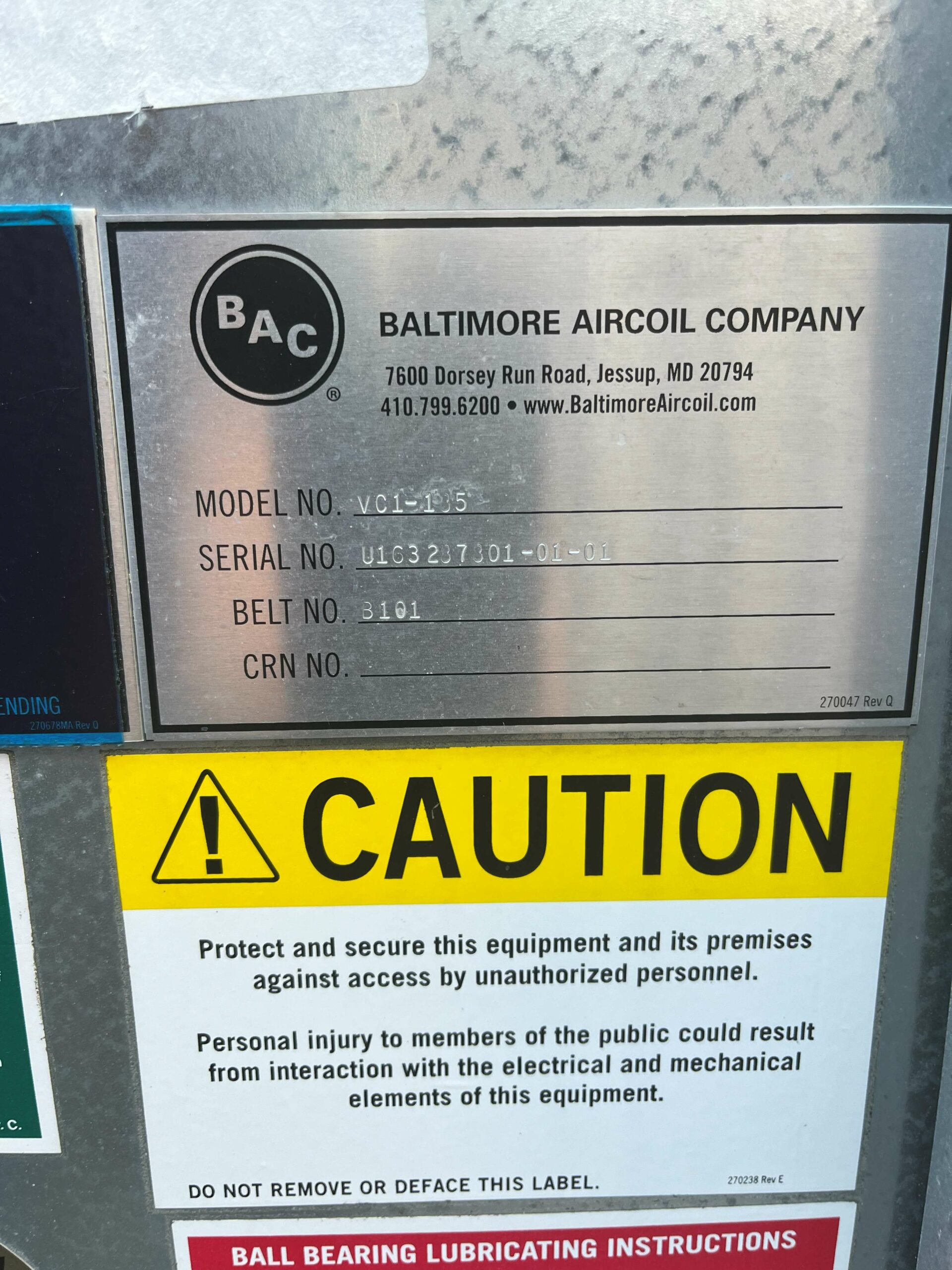 Metal nameplate on industrial equipment showing Baltimore Aircoil Company (BAC) logo and contact info, model VC1-15, serial number U163237301-01-01, belt number 3101, with a yellow CAUTION sign beneath.