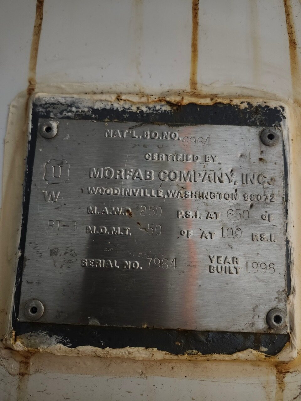 Metal identification plate on a weathered device, showing Serial No. 7964 and Year Built 1998, from Morfab Company, Inc.