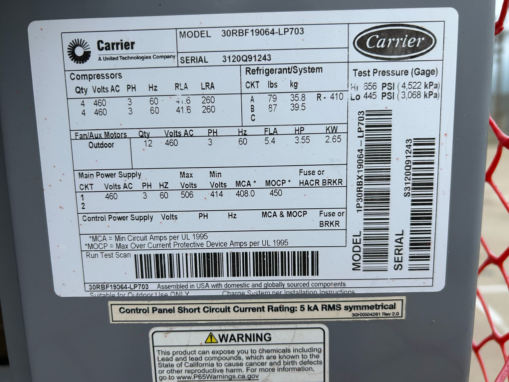 Industrial equipment nameplate with Carrier logo and model/serial numbers, plus electrical specifications and warnings visible on a gray surface.