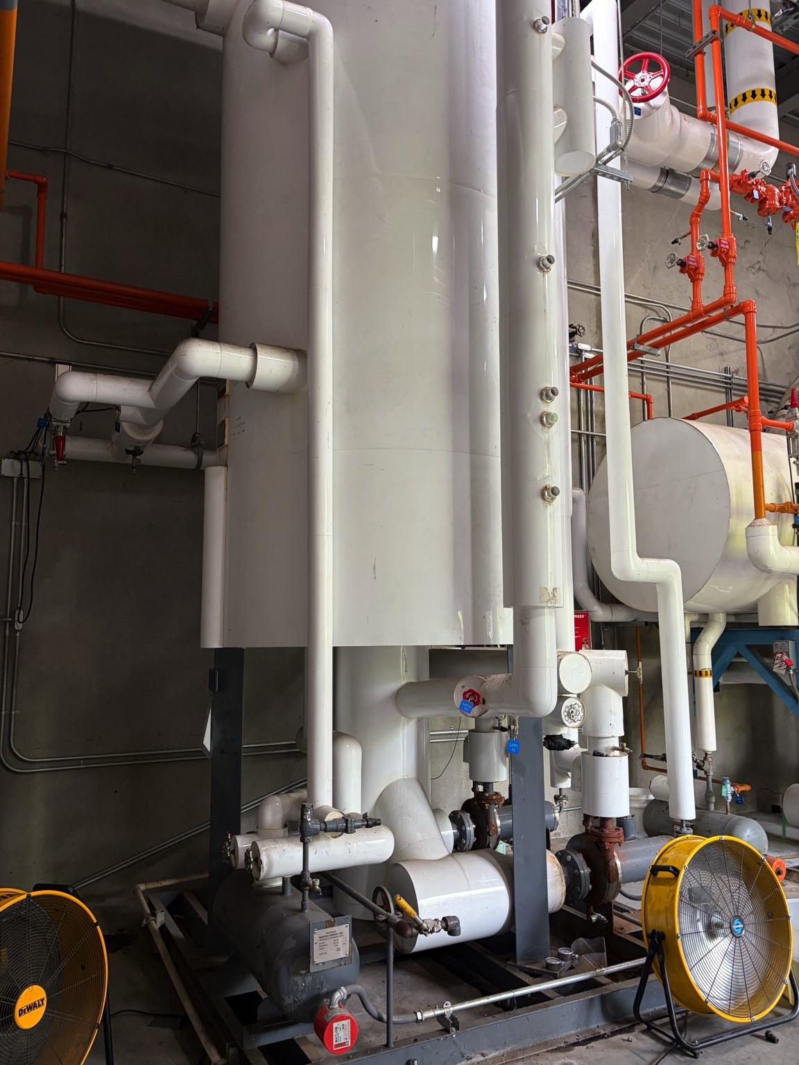Industrial mechanical room with large white insulated pipes, valves, and pumps network for a utility system.
